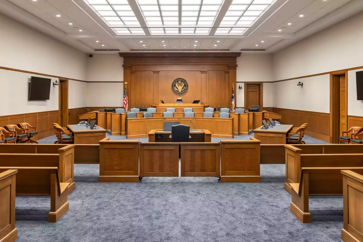 Una sala de tribunal vacía con asientos de madera y un estrado del juez.