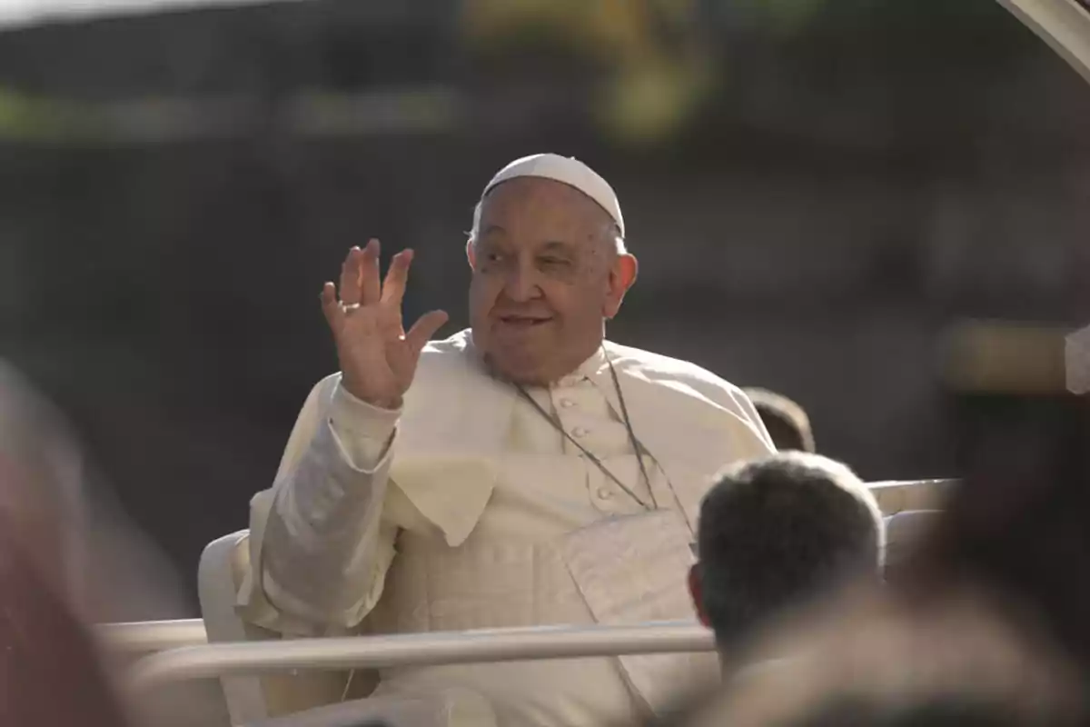 El papa Francisco saluda mientras está sentada en un vehículo descubierto.