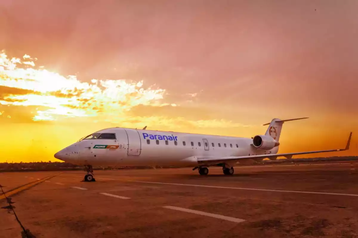 Un avión de Paranair estacionado en una pista al atardecer con un cielo anaranjado y nubes dispersas.