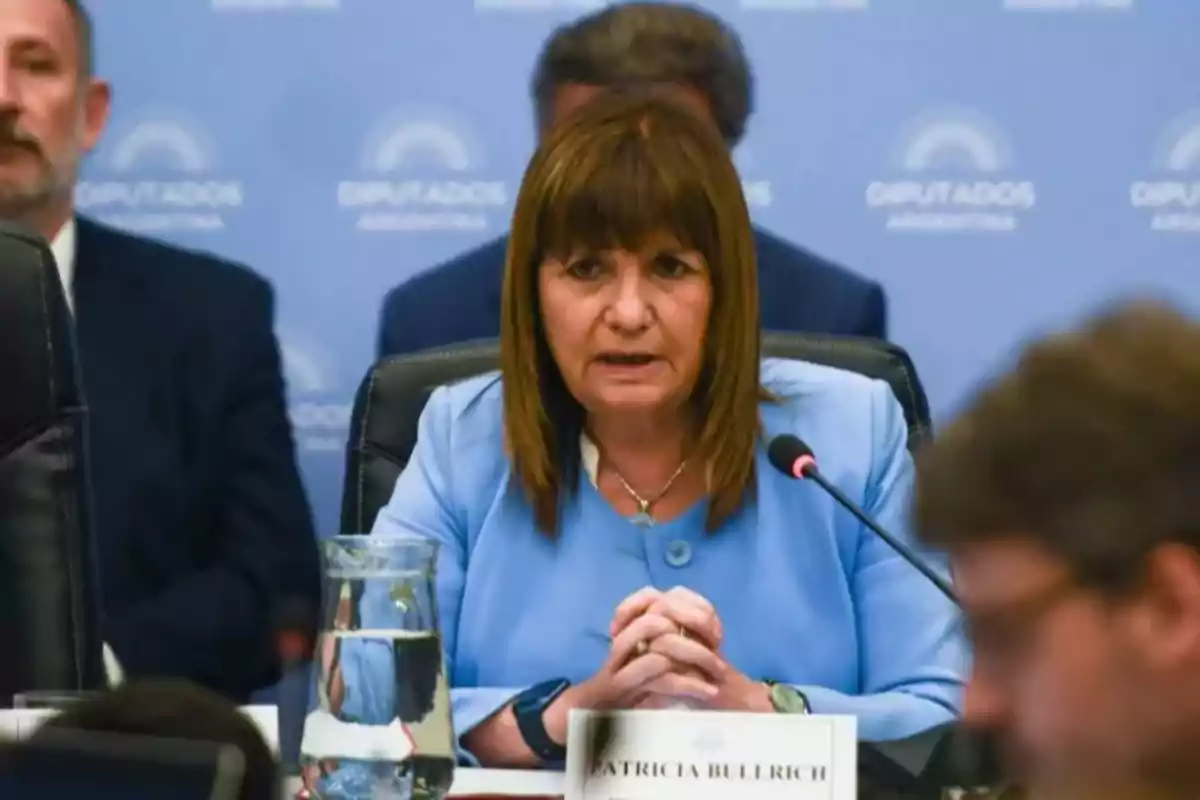 Una mujer hablando en una conferencia con un micrófono frente a ella y un cartel con su nombre.