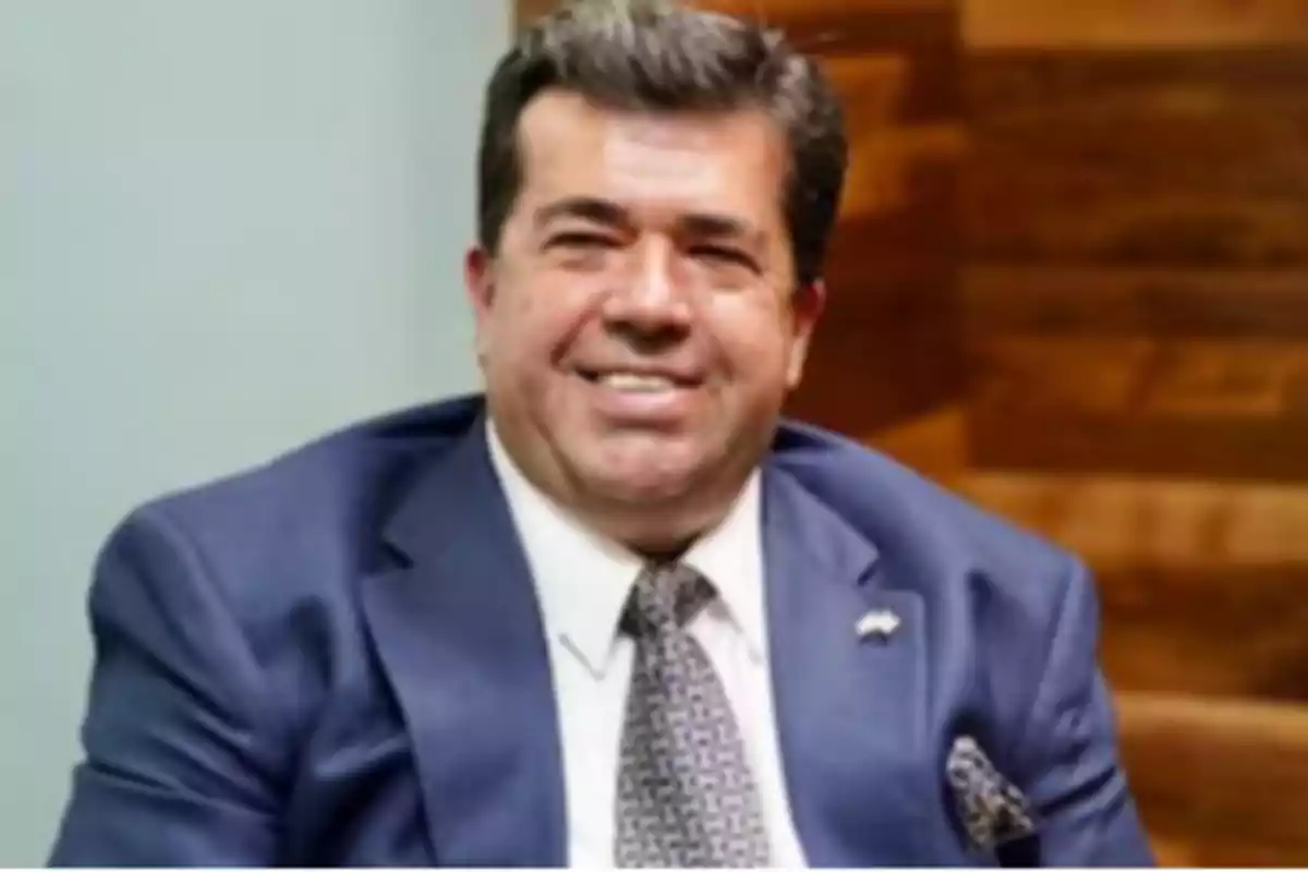 A man in a blue suit and tie smiles while sitting.