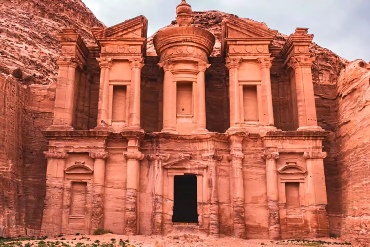 Una estructura antigua tallada en roca con columnas y detalles arquitectónicos en un entorno montañoso.