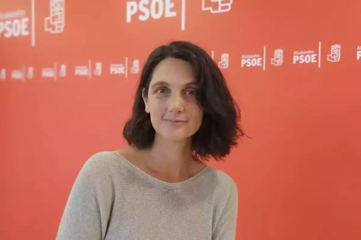 Mujer de cabello oscuro frente a un fondo rojo con logotipos del PSOE.