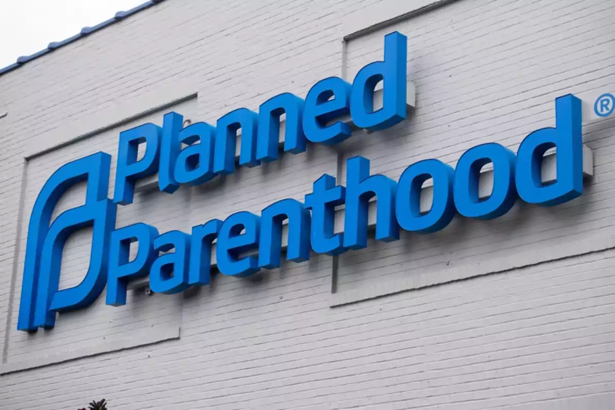 A blue Planned Parenthood sign on the wall of a white building.