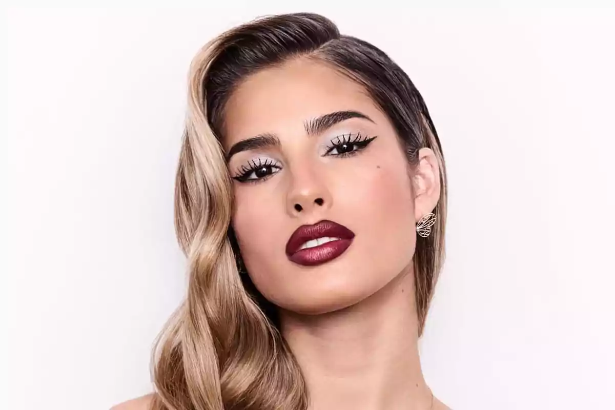 A person with elegant makeup and dark lips posing in front of a white background.