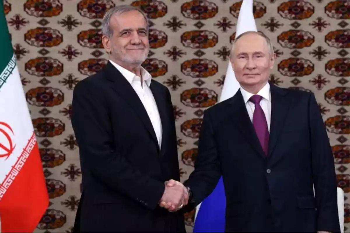 Dos hombres de traje se dan la mano frente a banderas de Irán y Rusia.