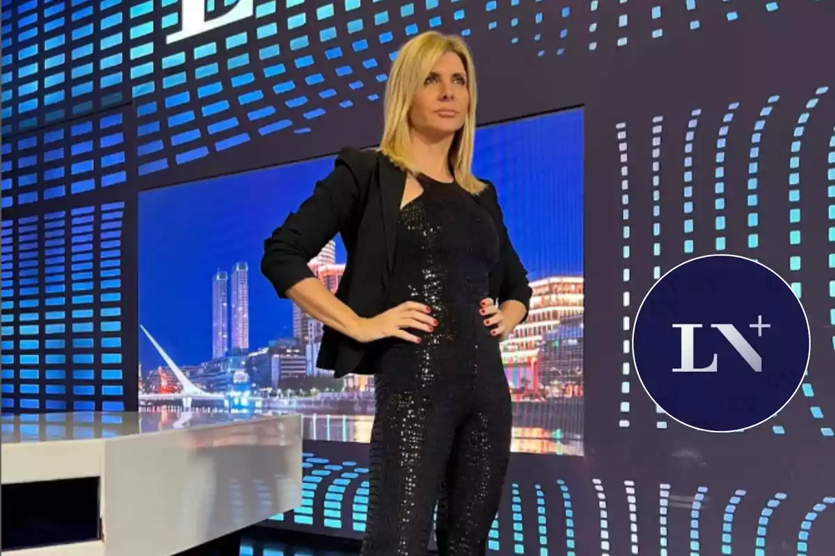 Mujer rubia con traje negro brillante en un set de televisión con fondo de ciudad iluminada y logotipo de LN+ en la esquina.