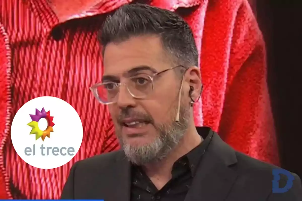 Un hombre con gafas y barba hablando en un programa de televisión con el logo de "el trece" en la esquina.