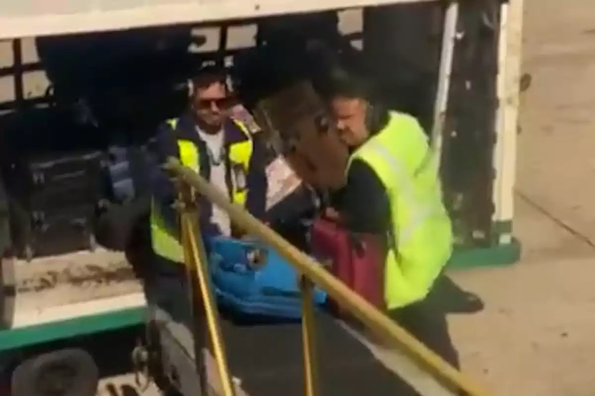 Dos trabajadores de aeropuerto manejan equipaje en una cinta transportadora.