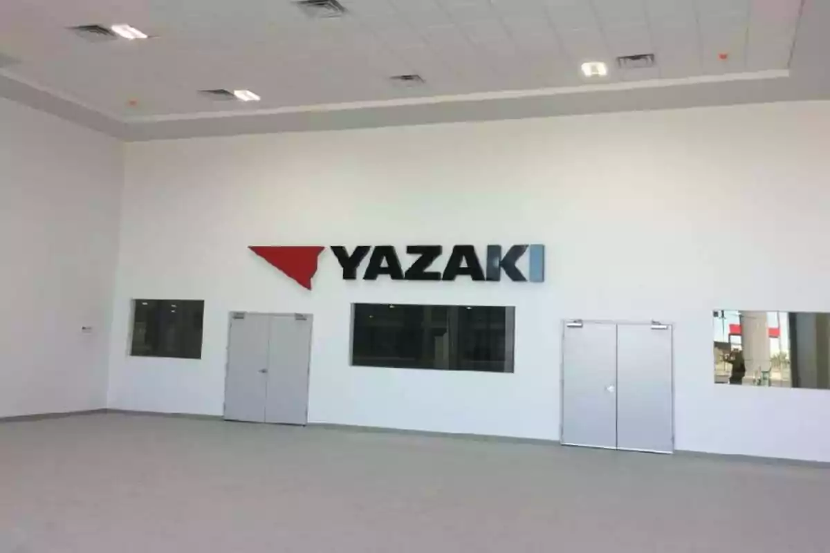 Un gran salón vacío con un logotipo de Yazaki en la pared blanca y varias puertas y ventanas.