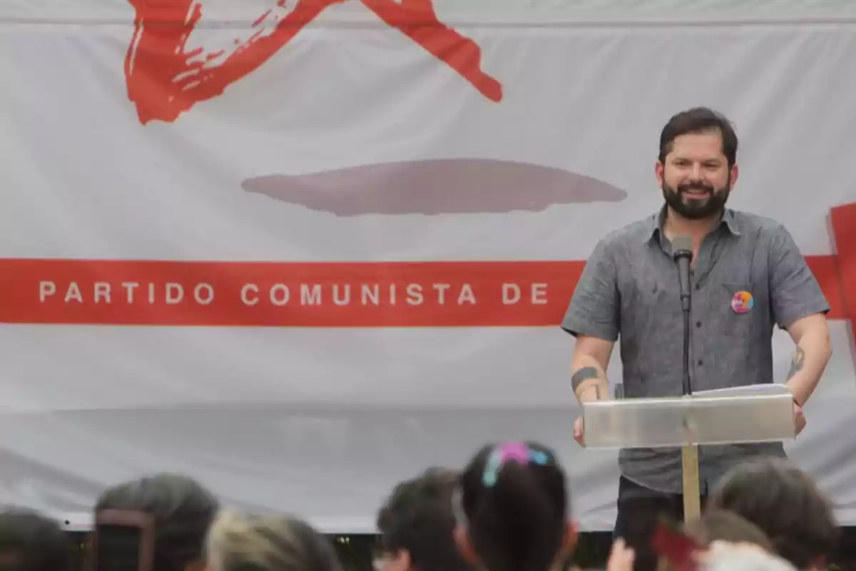 Un hombre hablando en un podio frente a un cartel del Partido Comunista.