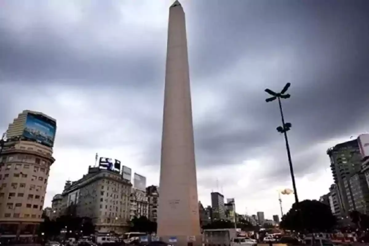 Obelisco en una avenida concurrida con edificios y cielo nublado.