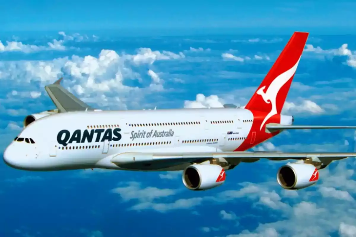 Avión de la aerolínea Qantas volando sobre un cielo azul con nubes.