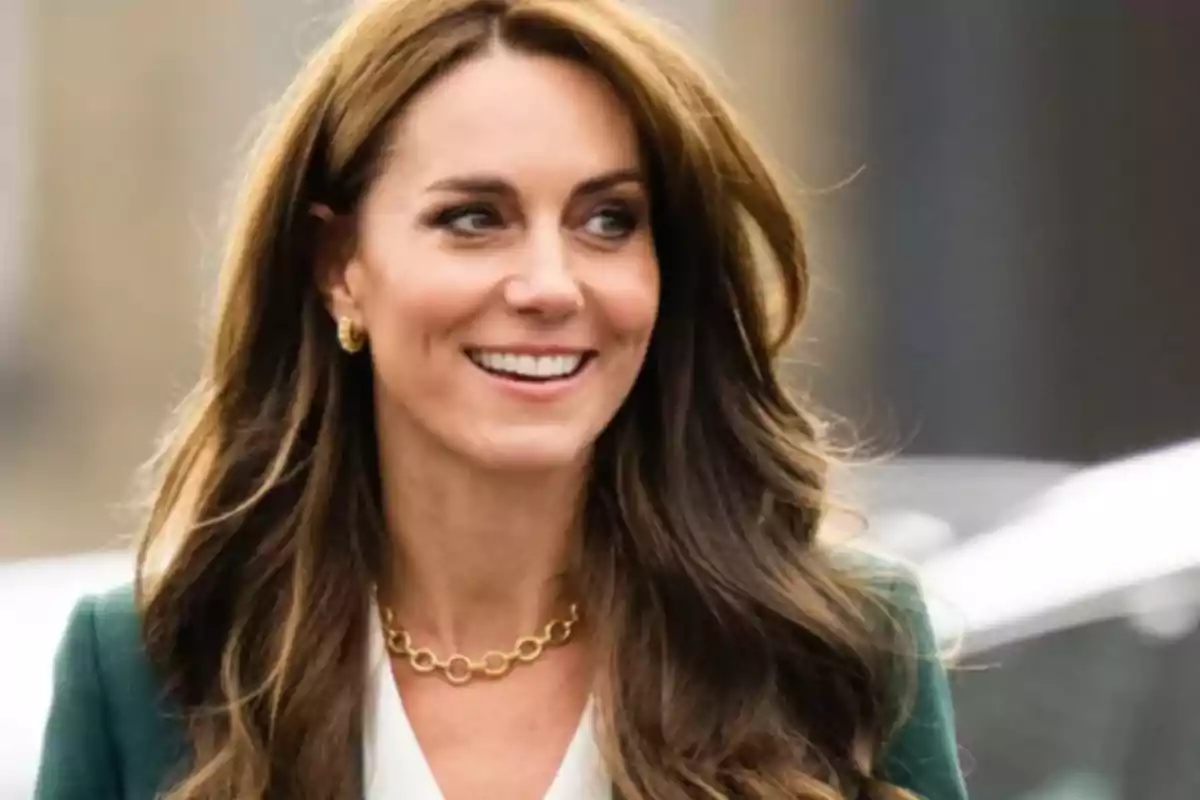 Una mujer con cabello largo y castaño sonriendo mientras lleva un collar dorado y un atuendo elegante.