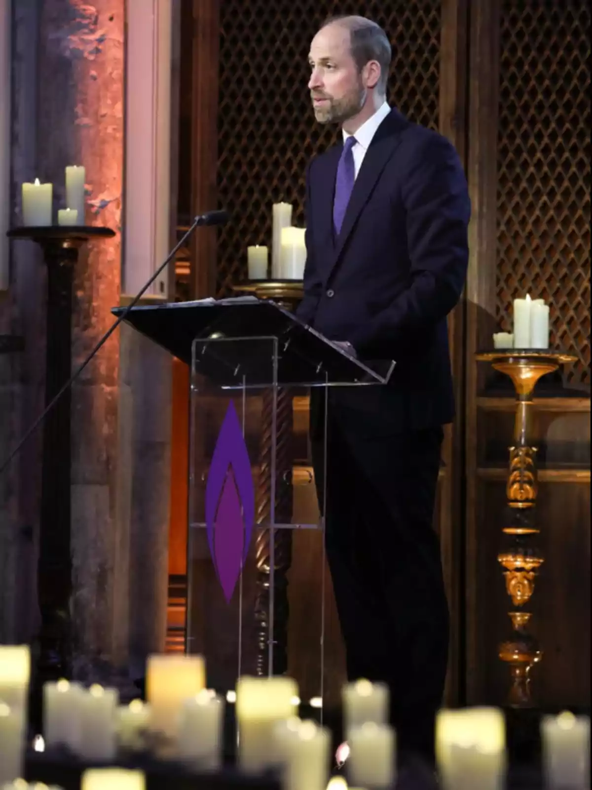 Un hombre de pie en un podio hablando en un evento con velas encendidas alrededor.