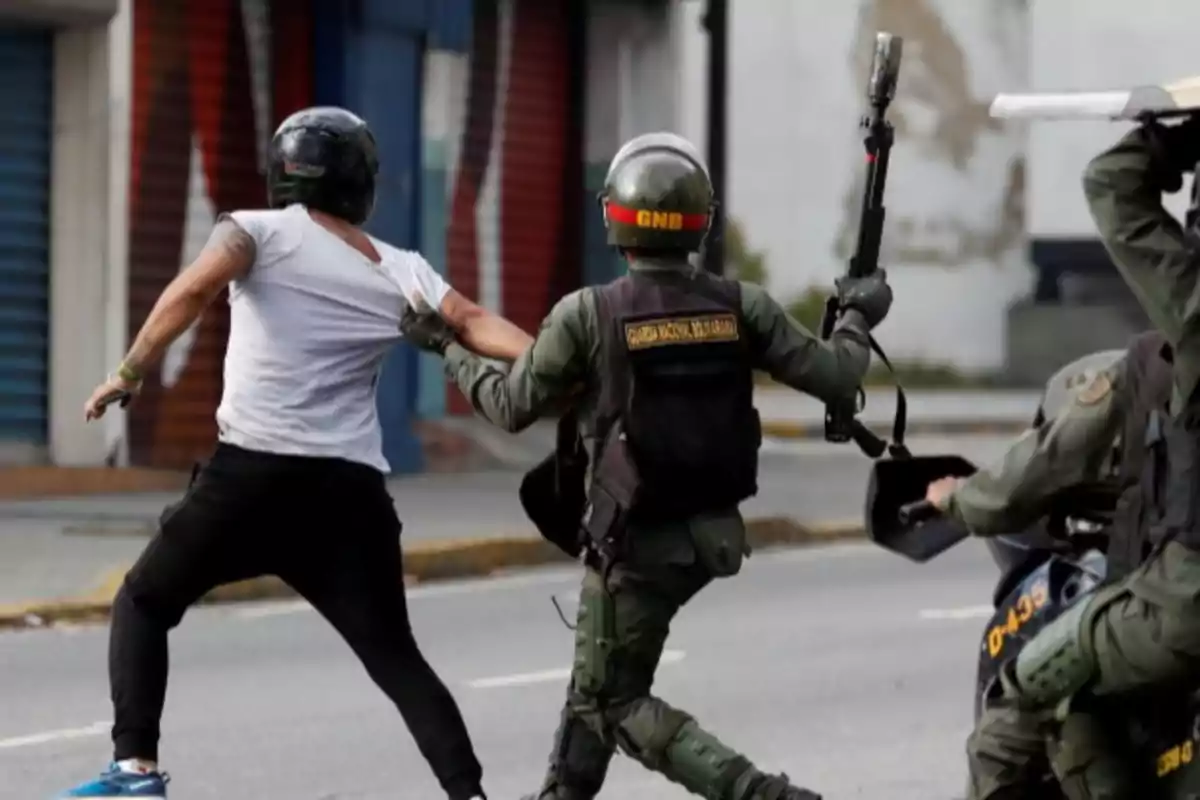 Un oficial de la Guardia Nacional Bolivariana detiene a un manifestante en una calle.