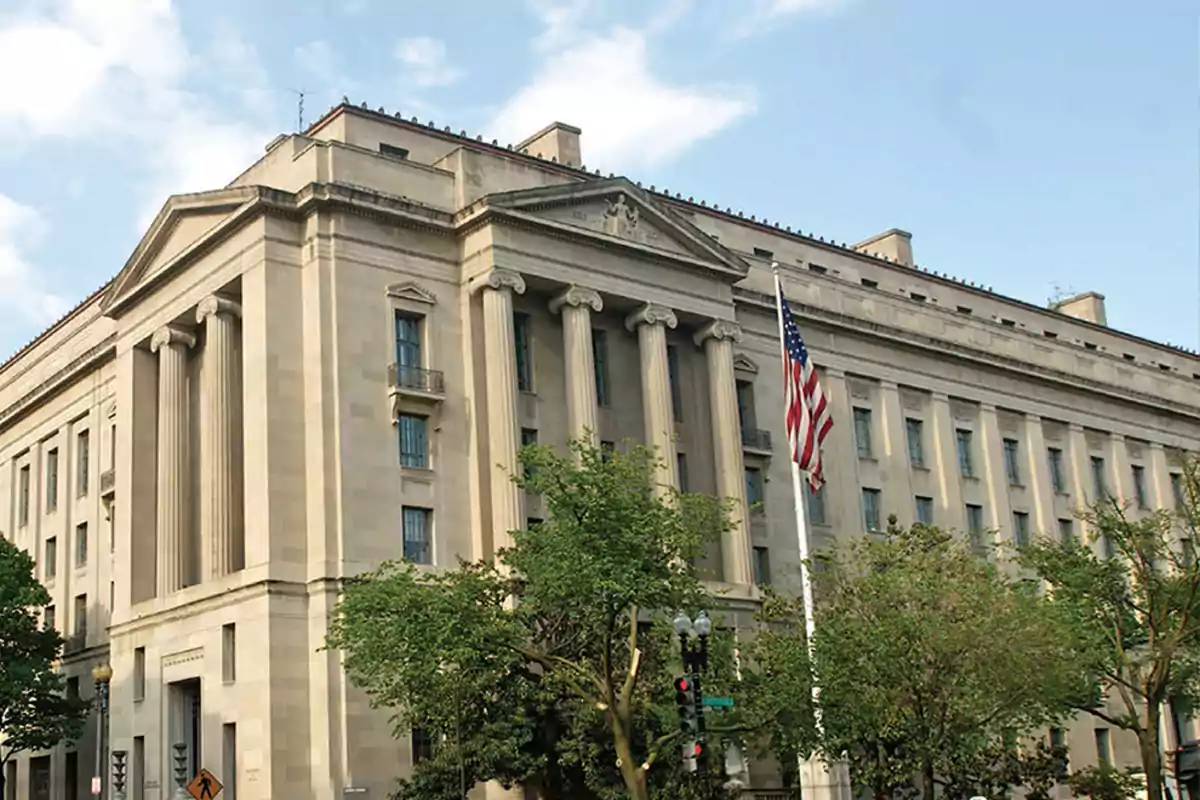 Edificio gubernamental con columnas clásicas y una bandera de Estados Unidos ondeando al frente.