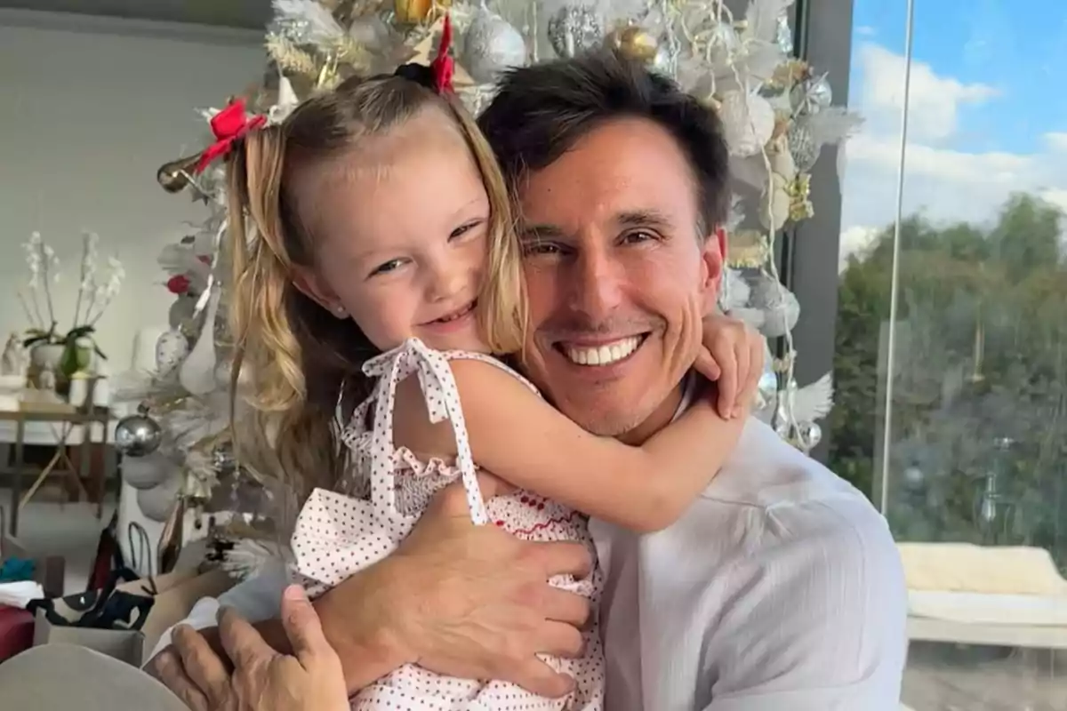 Un hombre y una niña sonríen mientras se abrazan frente a un árbol de Navidad decorado.