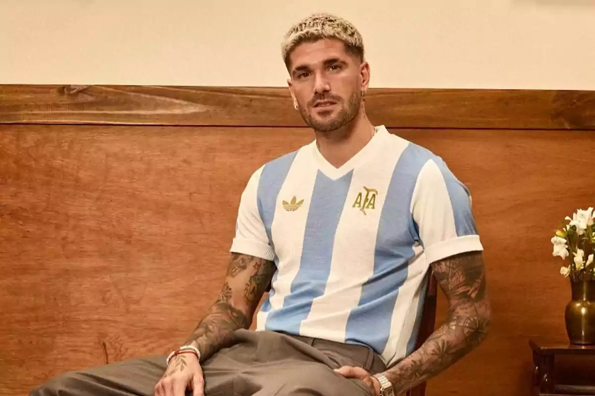 A man wearing an Argentina soccer jersey sitting on a wooden chair.