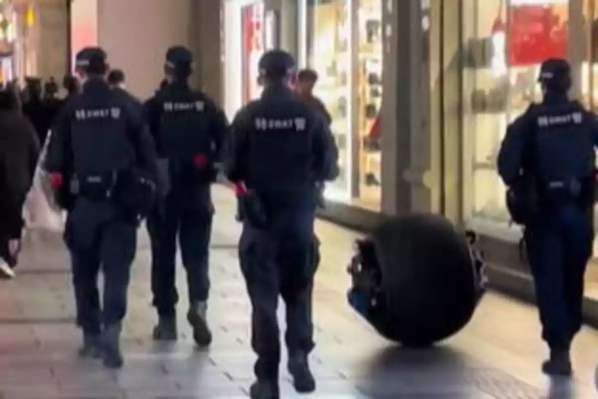 Un grupo de policías camina por una calle comercial junto a un robot con forma de rueda.