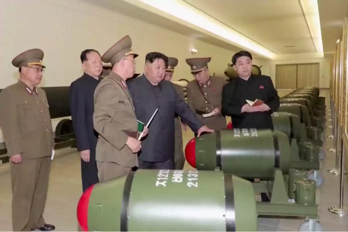 Un grupo de hombres en uniforme militar observa una fila de objetos cilíndricos verdes en una sala iluminada.