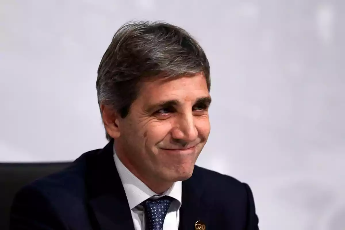 Un hombre de cabello canoso y traje oscuro sonríe mientras está sentado frente a un fondo claro.