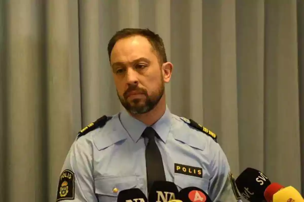 Un hombre con uniforme de policía frente a varios micrófonos.