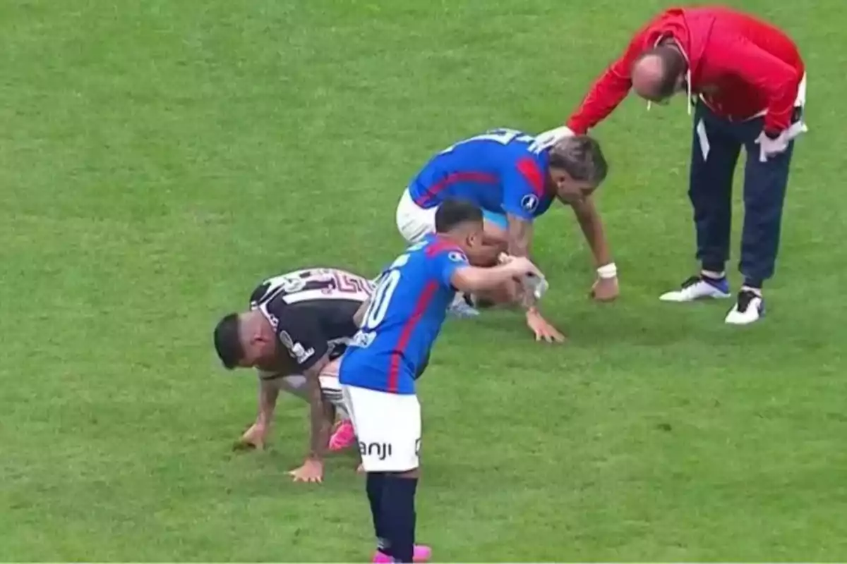 Jugadores de fútbol y un entrenador en el campo, algunos de ellos agachados y uno recibiendo atención.