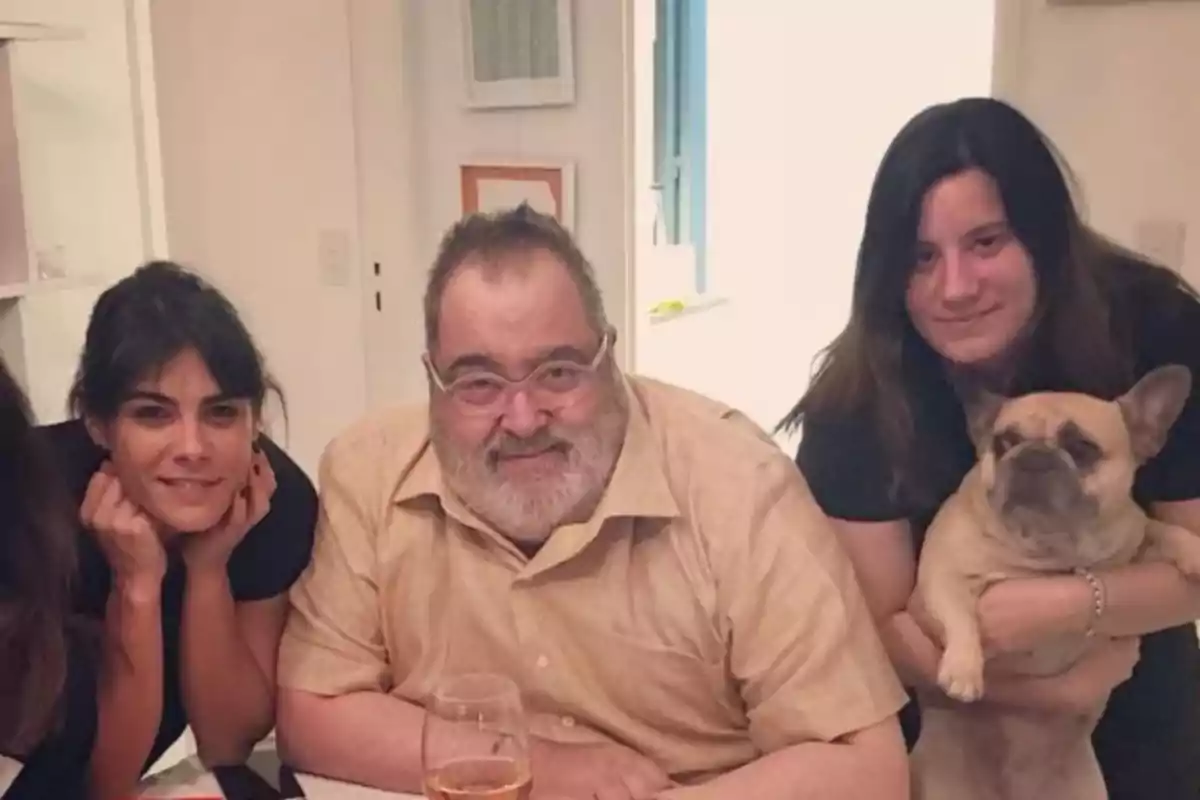 Un grupo de personas sonríe mientras posan alrededor de una mesa, una de ellas sostiene un perro pequeño.