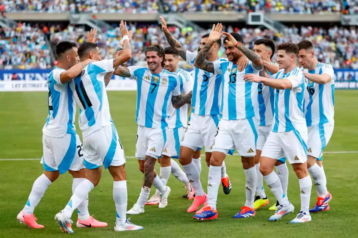 Jugadores de fútbol con uniformes de rayas celestes y blancas celebran en el campo de juego.