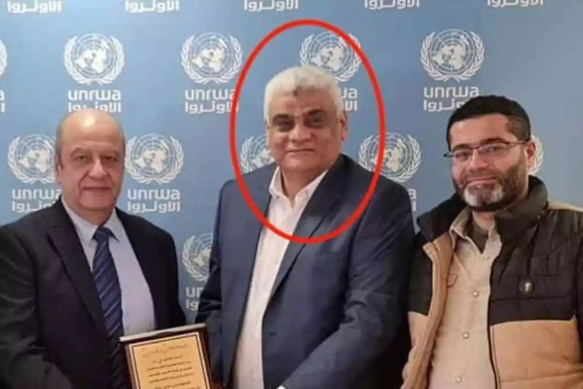 Tres hombres posan frente a un fondo con el logotipo de la UNRWA, uno de ellos está rodeado por un círculo rojo.