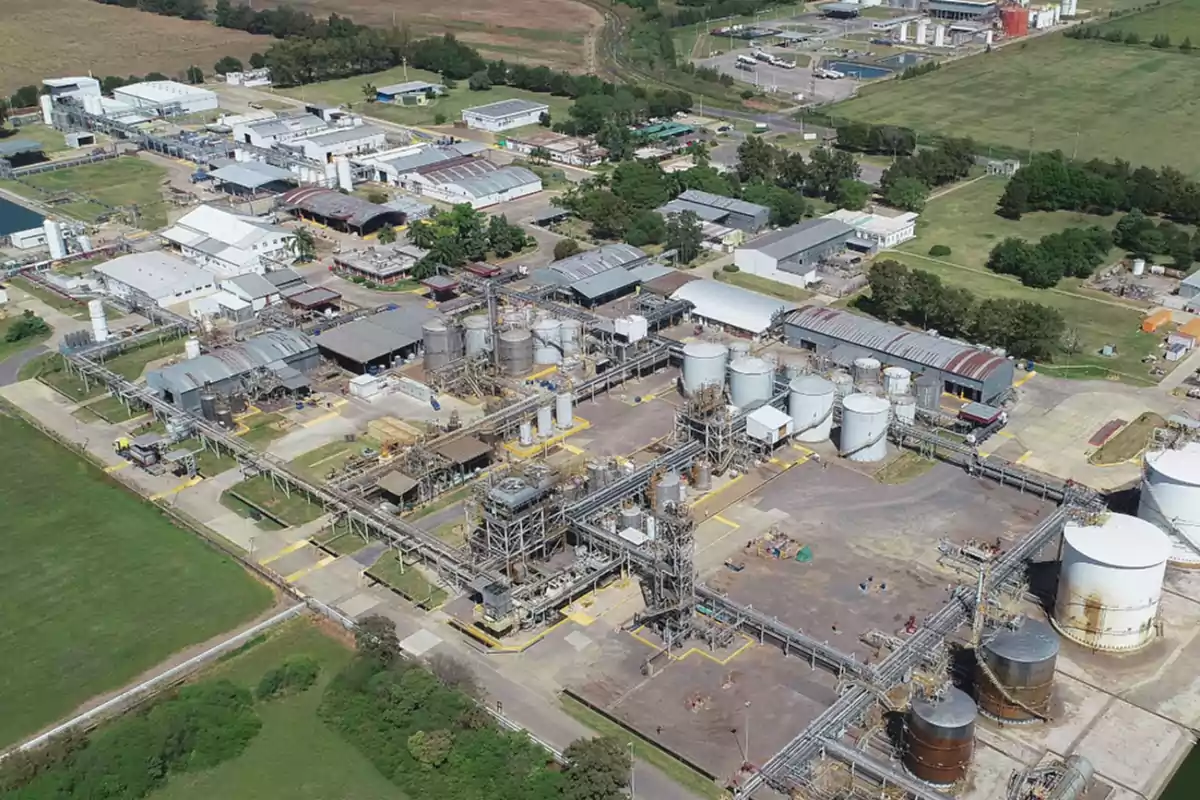 Vista aérea de una planta industrial con varios edificios, tanques de almacenamiento y áreas verdes alrededor.