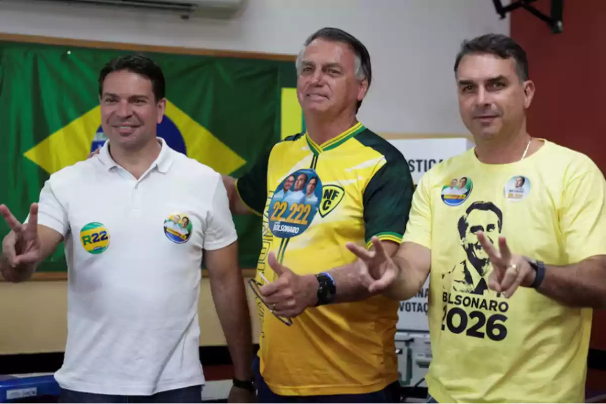 Tres hombres posan frente a una bandera de Brasil haciendo el signo de la paz con las manos y llevan camisetas con insignias políticas.