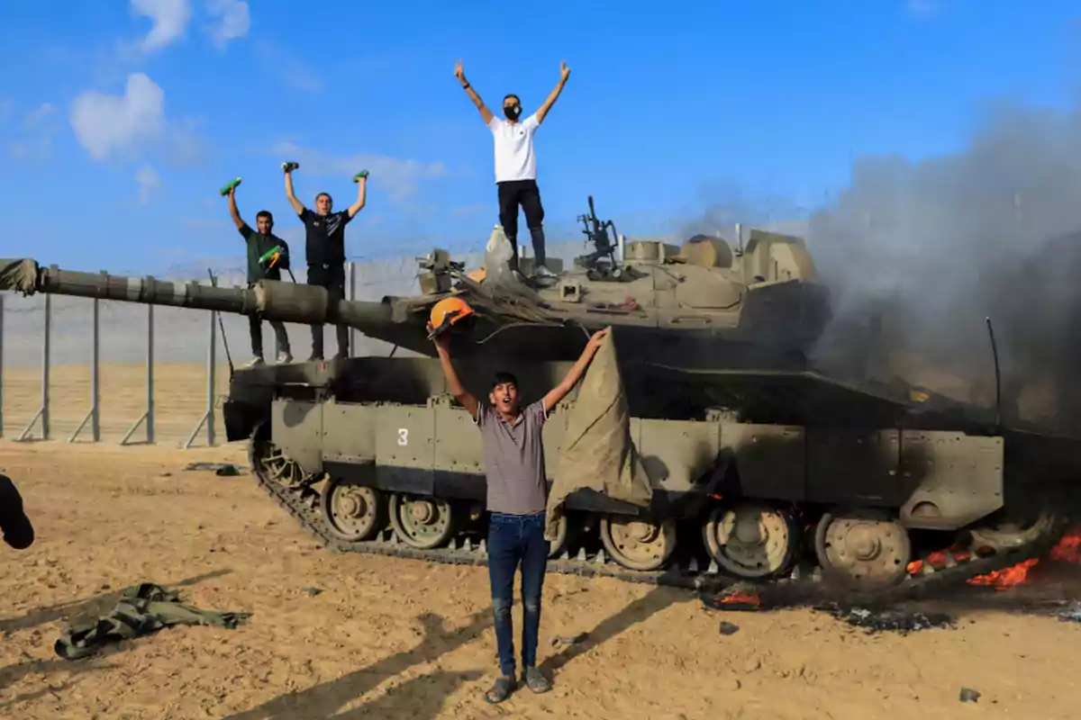 Personas celebrando sobre un tanque en un área desértica con humo alrededor.