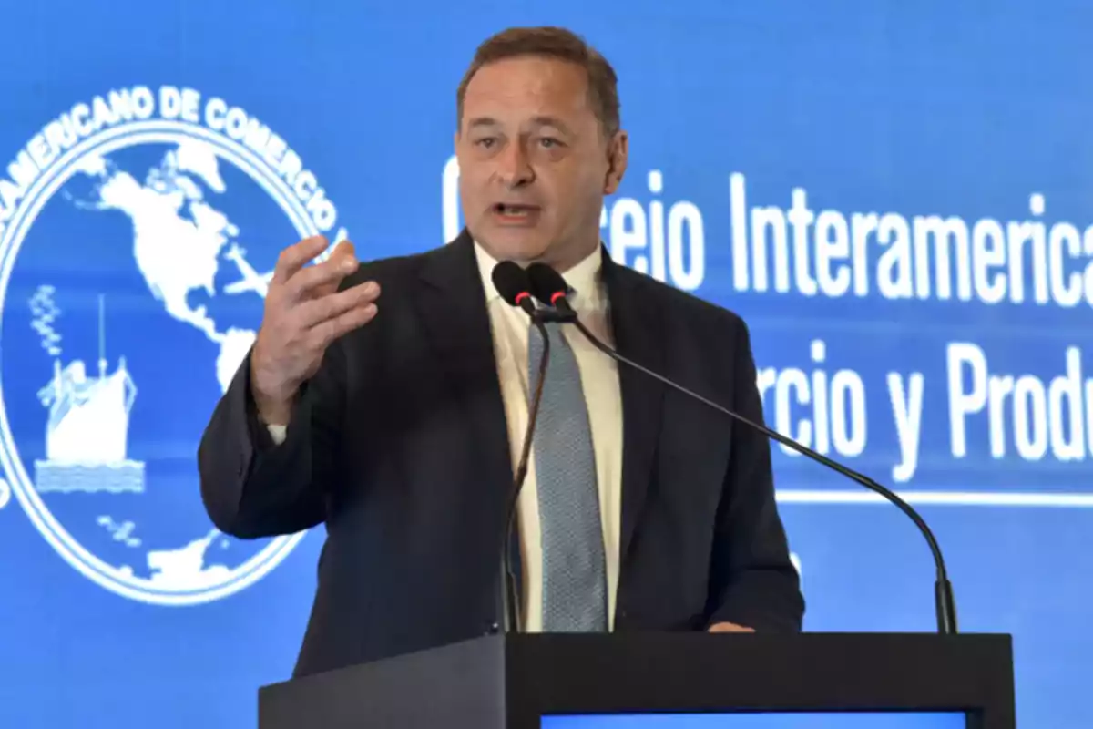 Un hombre en traje hablando en un podio con un fondo azul que muestra el logo del Consejo Interamericano de Comercio y Producción.