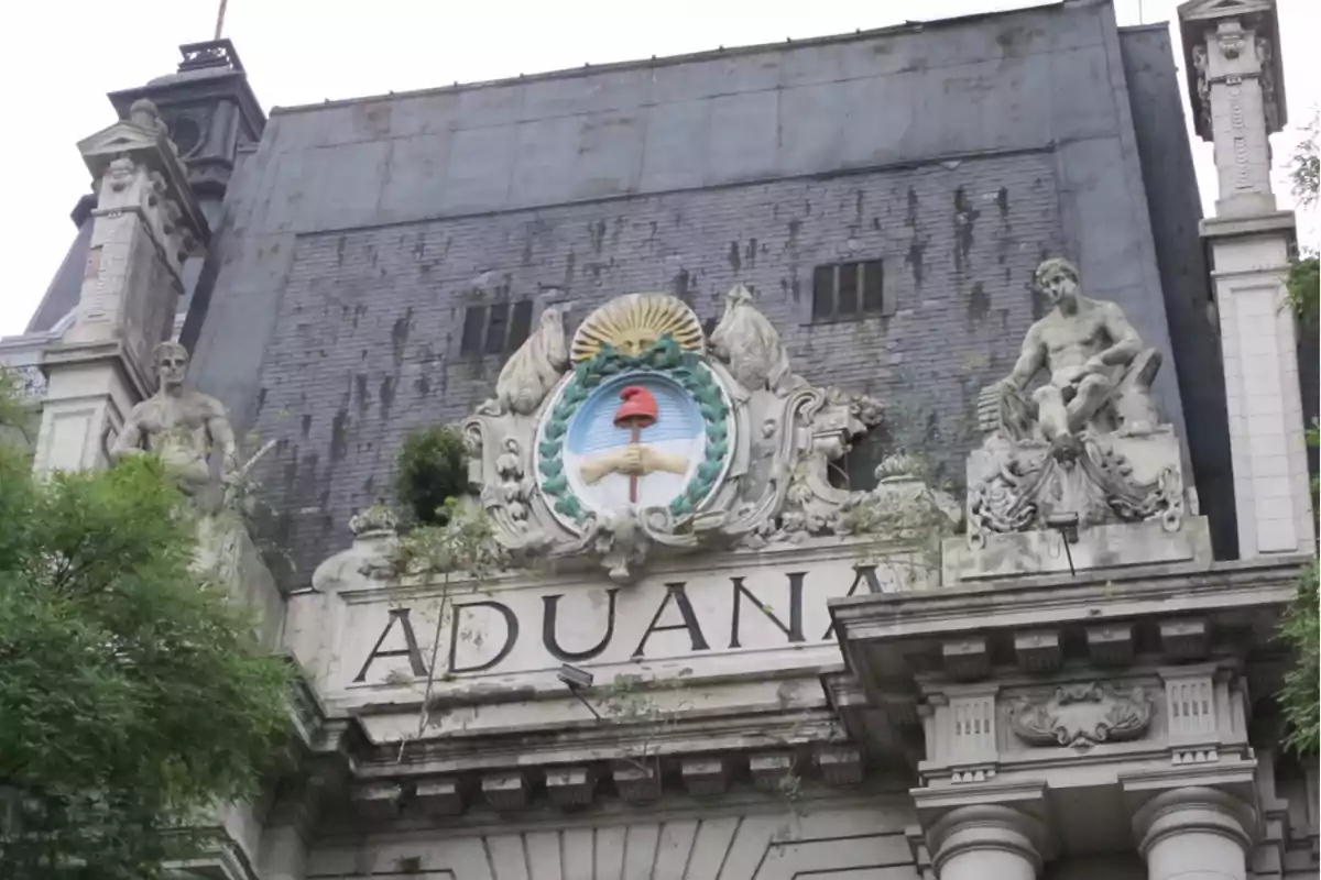 Fachada de un edificio antiguo con esculturas y un escudo decorativo que tiene la palabra "ADUANA" en la parte inferior.