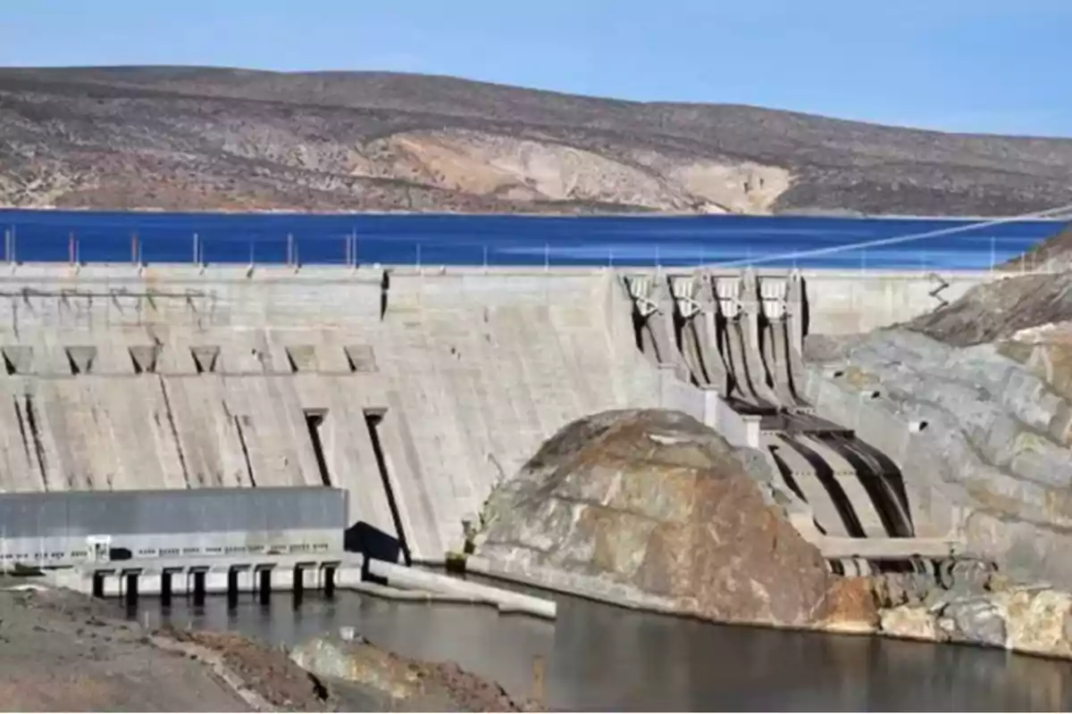 Vista de una presa de concreto con compuertas y un embalse en un paisaje árido.