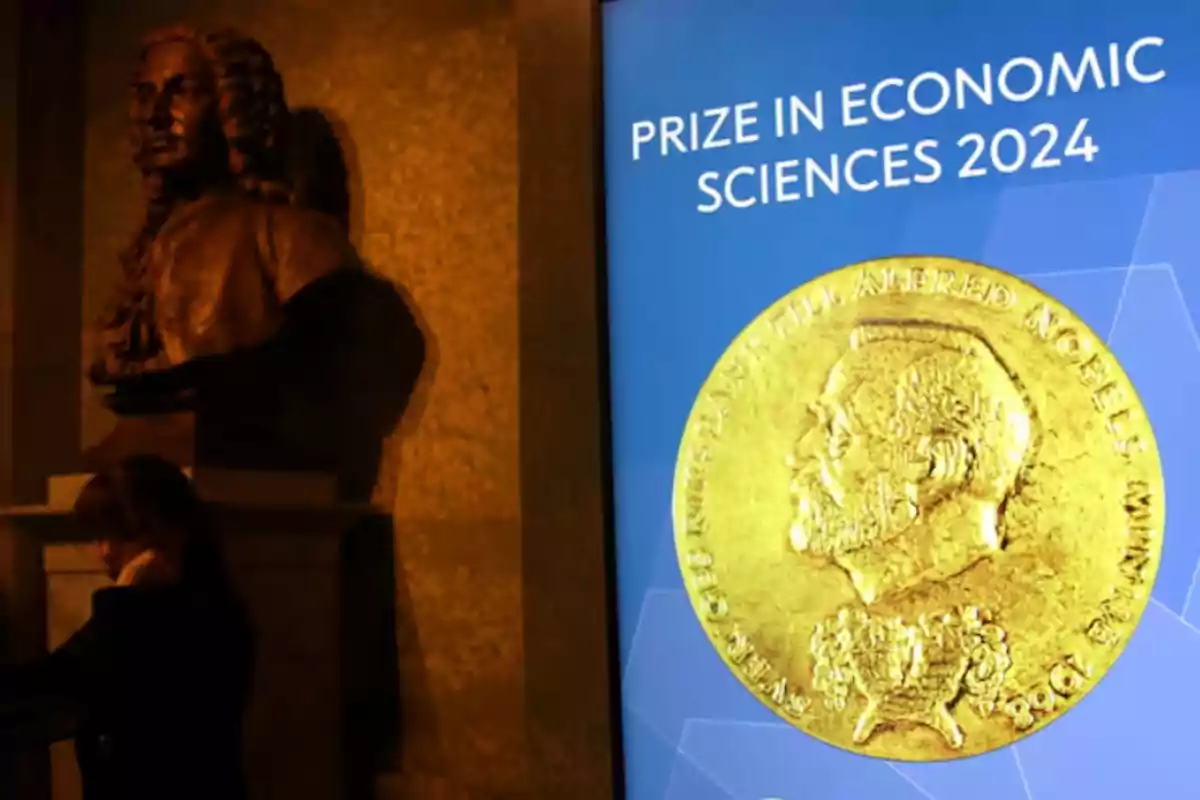 Una pantalla muestra el Premio en Ciencias Económicas 2024 junto a un busto en un entorno iluminado.