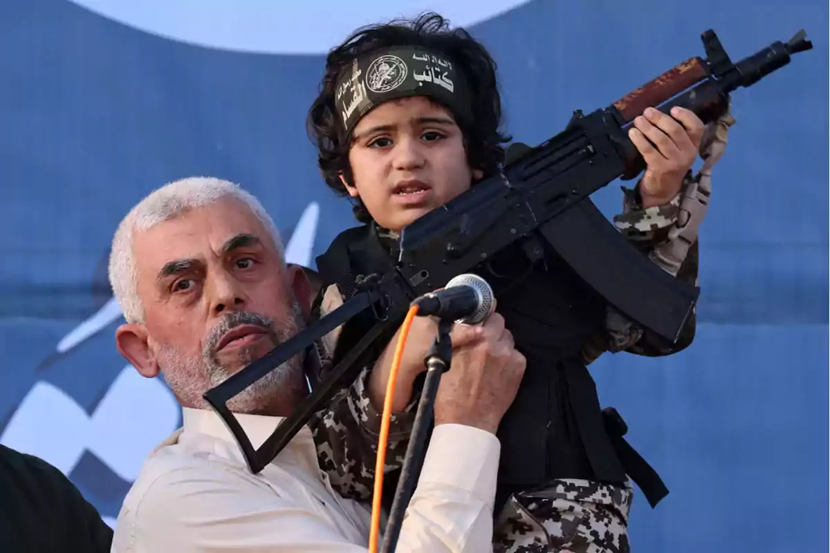 Un hombre sostiene a un niño vestido con uniforme militar y portando un arma durante un evento público.