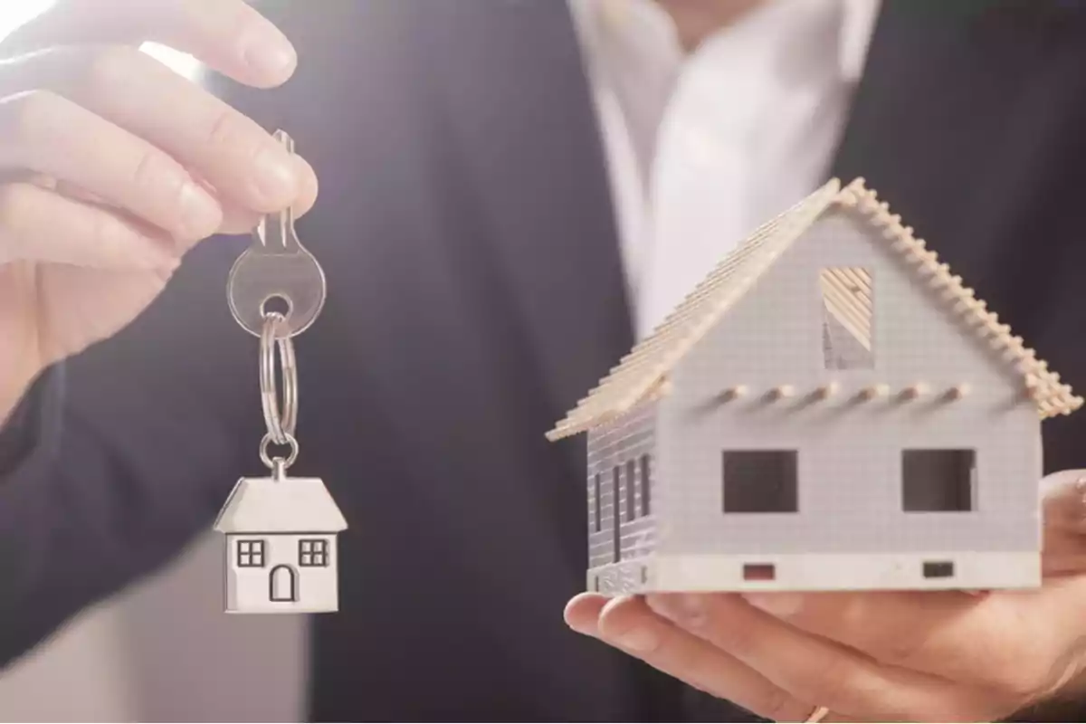 Persona sosteniendo una maqueta de casa en una mano y una llave con llavero de casa en la otra.