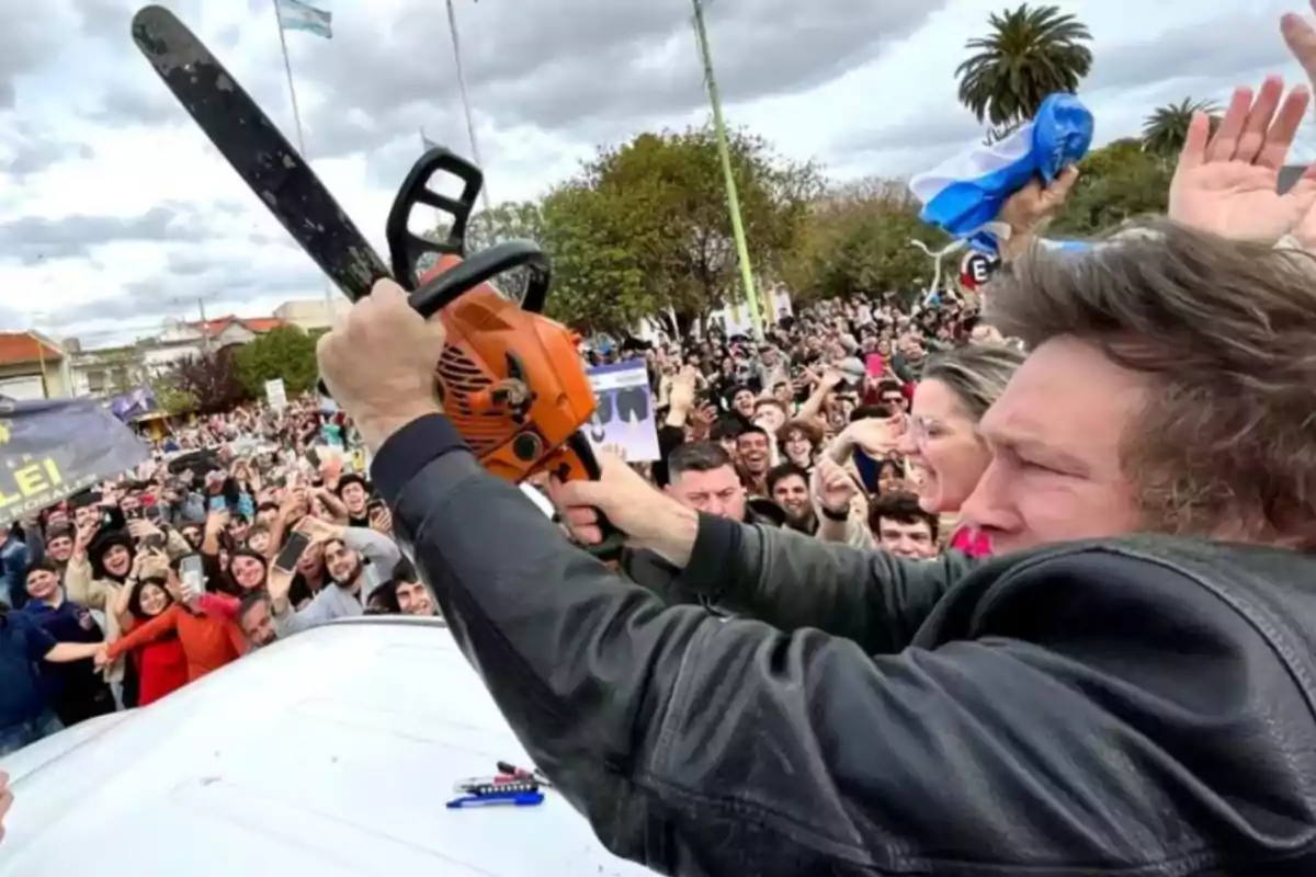 Una persona sostiene una motosierra en el aire frente a una multitud entusiasta en un evento al aire libre.