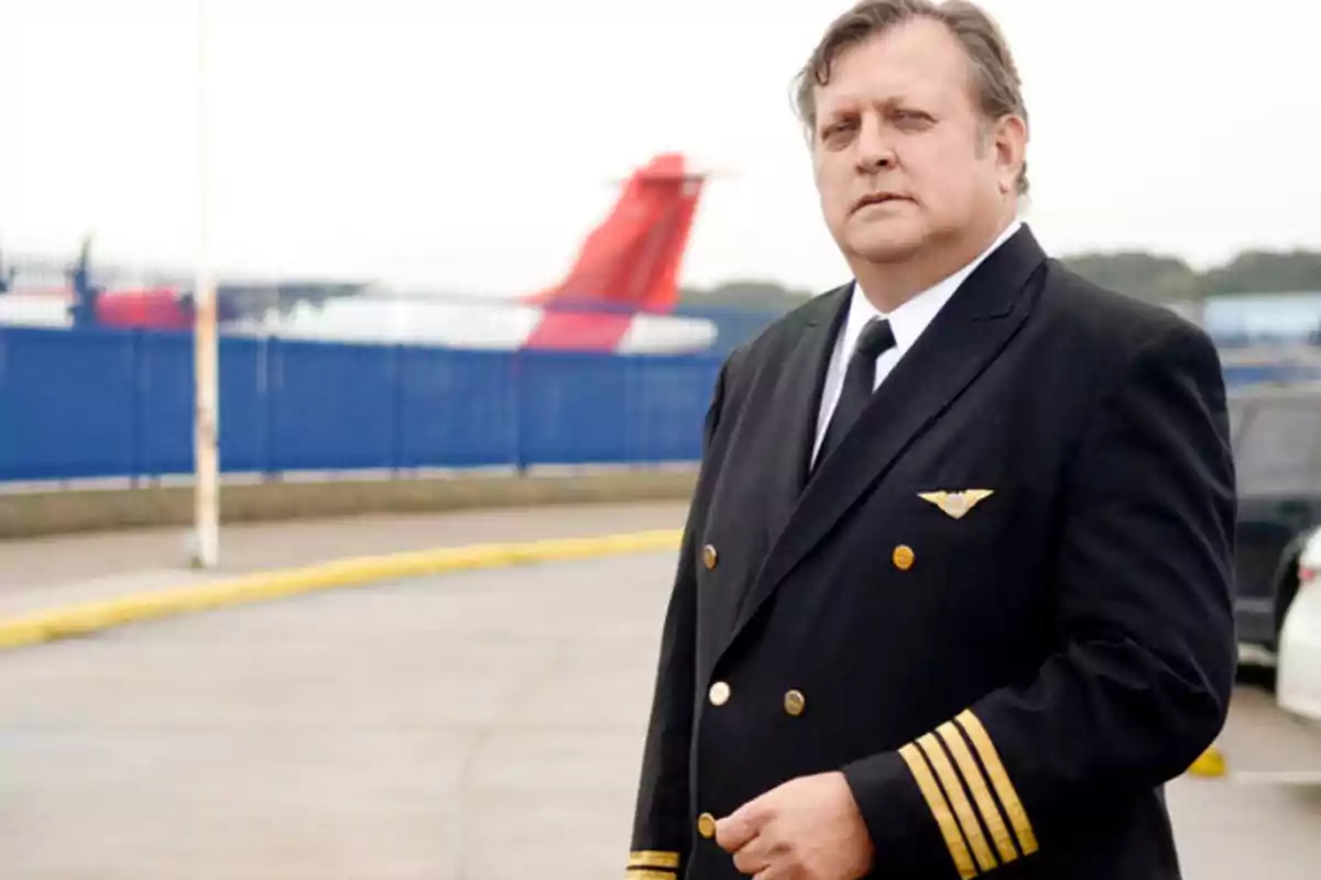 Un piloto de avión en uniforme de pie en una pista de aeropuerto con un avión en el fondo.