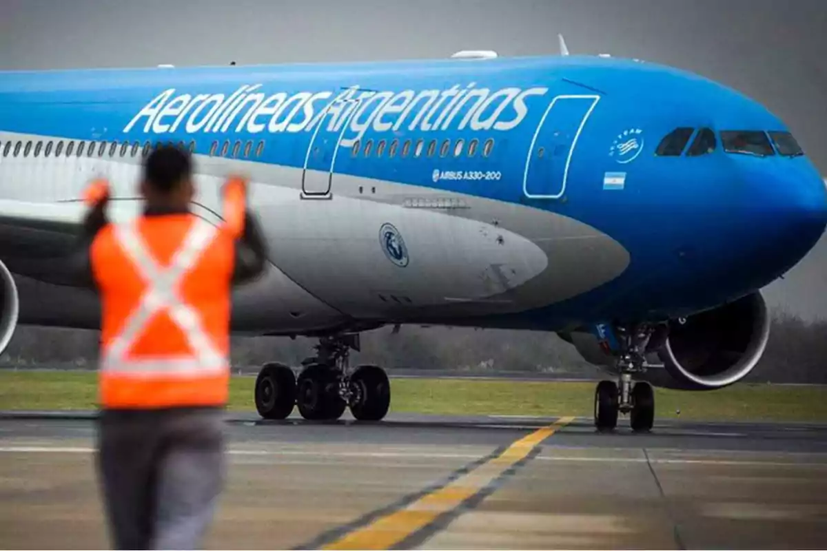 Un avión de Aerolíneas Argentinas en la pista con un trabajador de chaleco naranja guiándolo.