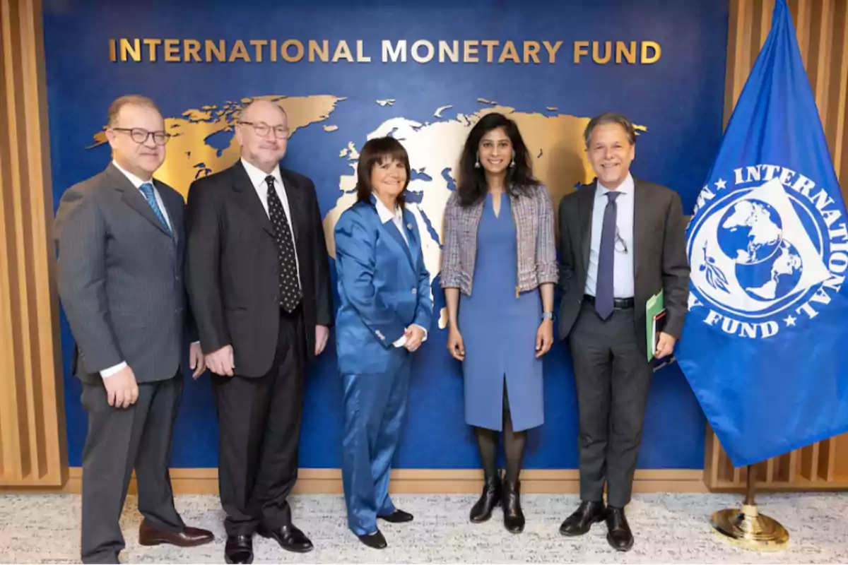 Un grupo de cinco personas posando frente a un fondo del Fondo Monetario Internacional con un mapa del mundo y una bandera a la derecha.