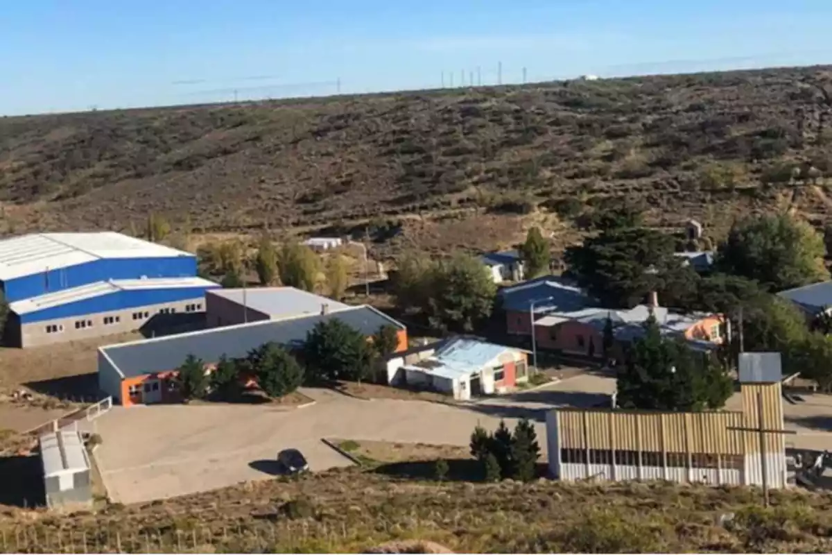 Vista aérea de un pequeño conjunto de edificios en una zona rural con colinas áridas al fondo.