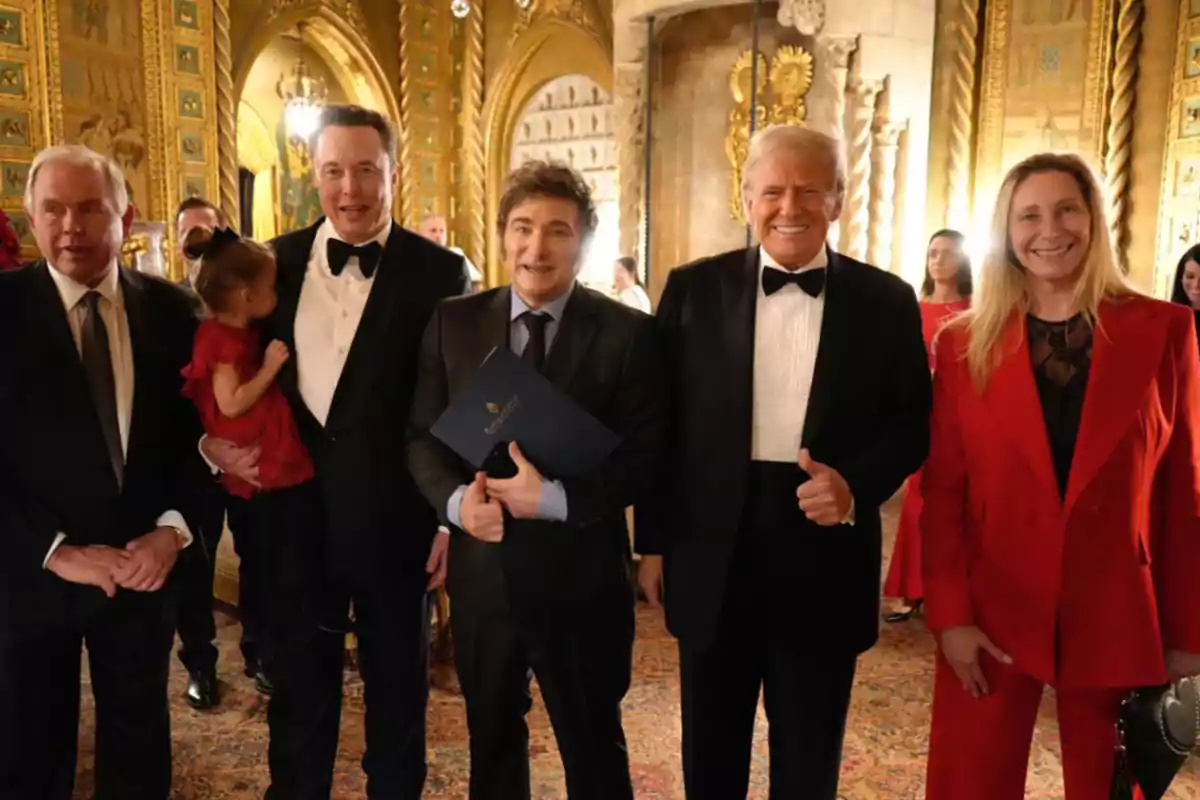 Un grupo de personas vestidas de manera formal posando en un elegante salón decorado con detalles dorados.