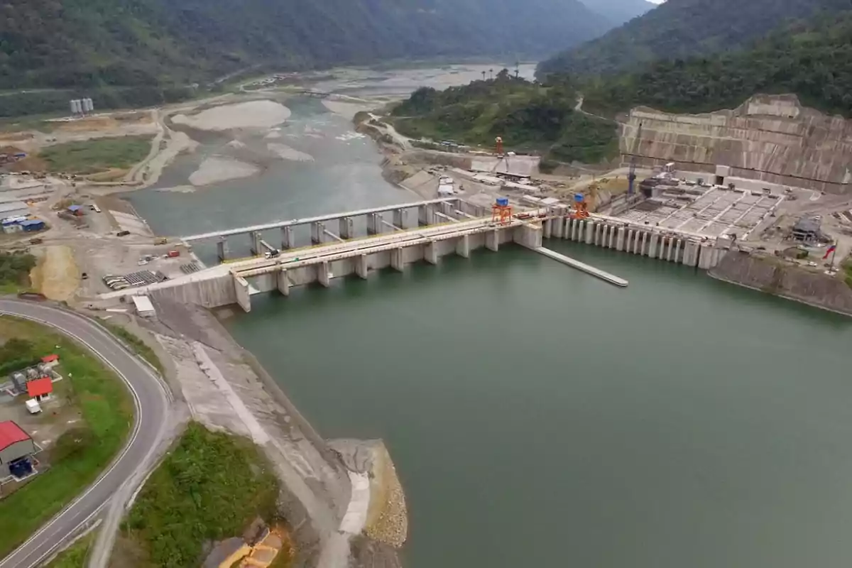 Vista aérea de una represa hidroeléctrica rodeada de montañas y vegetación con un río fluyendo a través de la estructura.