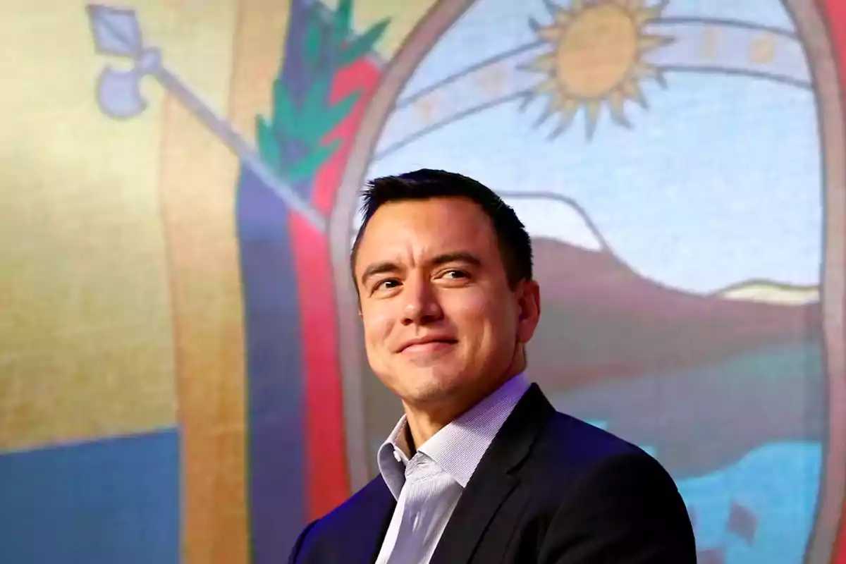 Un hombre sonriente con traje oscuro y camisa clara frente a un fondo colorido con un diseño de sol y montañas.