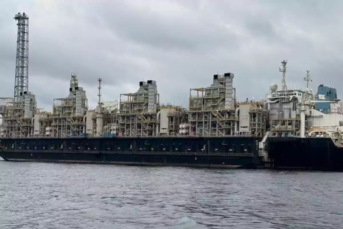 Un barco industrial grande en el agua con estructuras complejas y un cielo nublado de fondo.