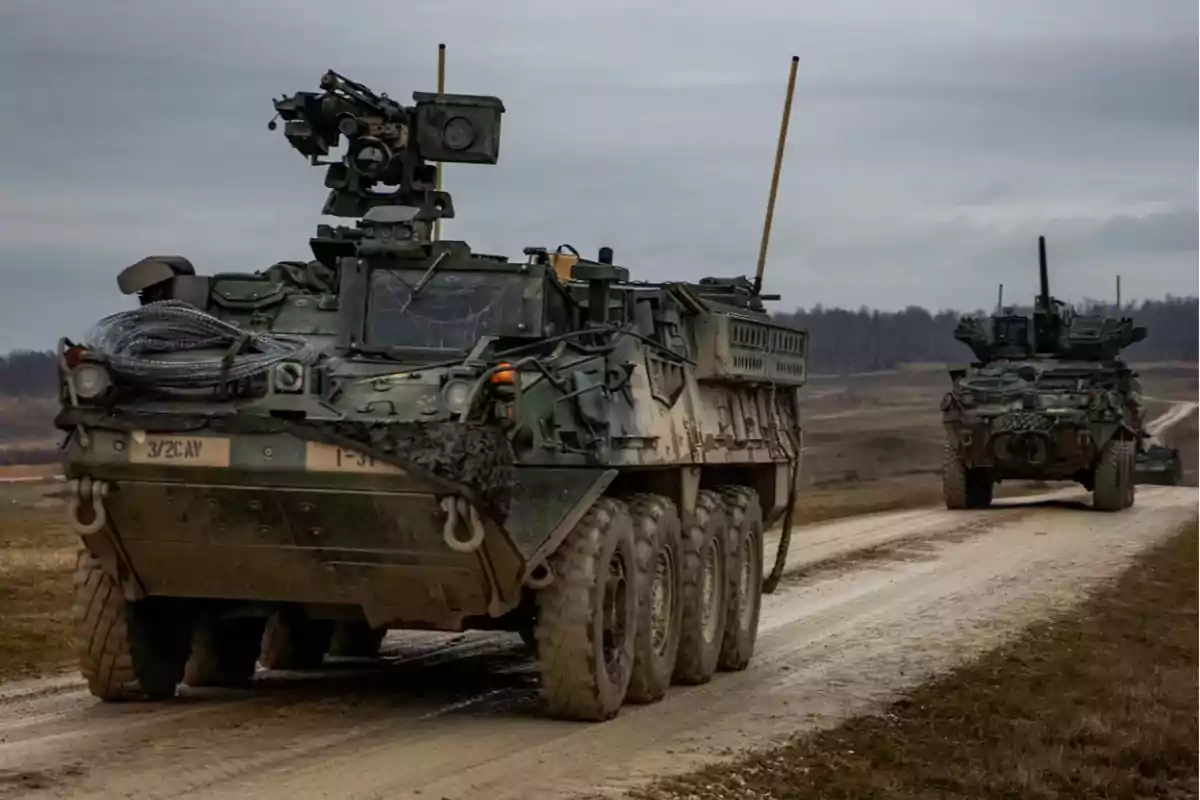 Vehículos militares blindados avanzando por un camino de tierra en un paisaje rural.